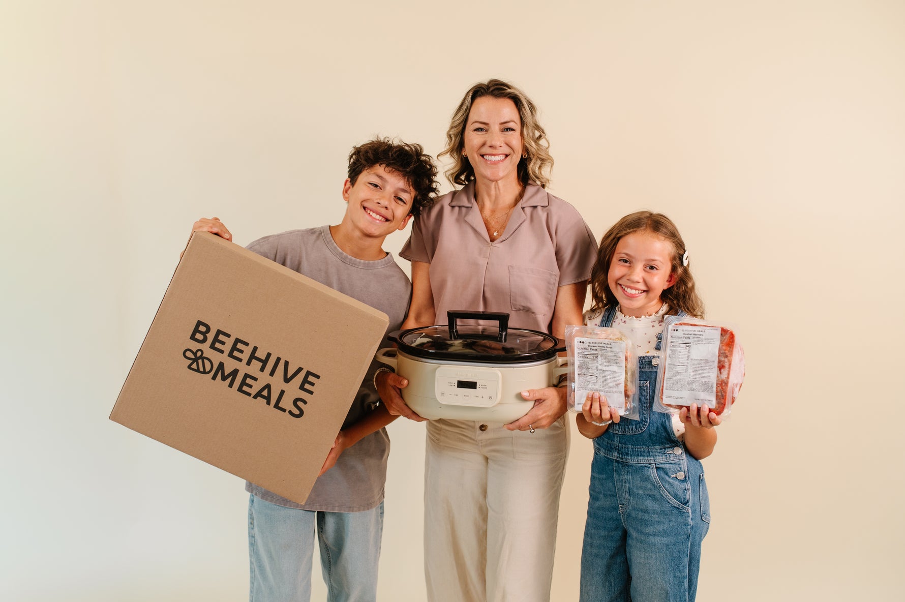 Mom and Kids carrying a Beehive Meals box, Beehive Meals meals, and a crockpot. 