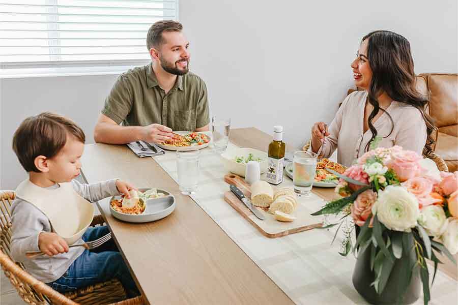 Family of three enjoying a meal together at a dining table with flowers and cutlery.