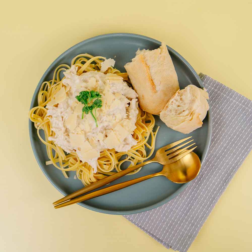 Plate of Beehive Meals Chicken Alfredo over fehttuchini noodles with bread and a gold fork and spoon on a yellow background