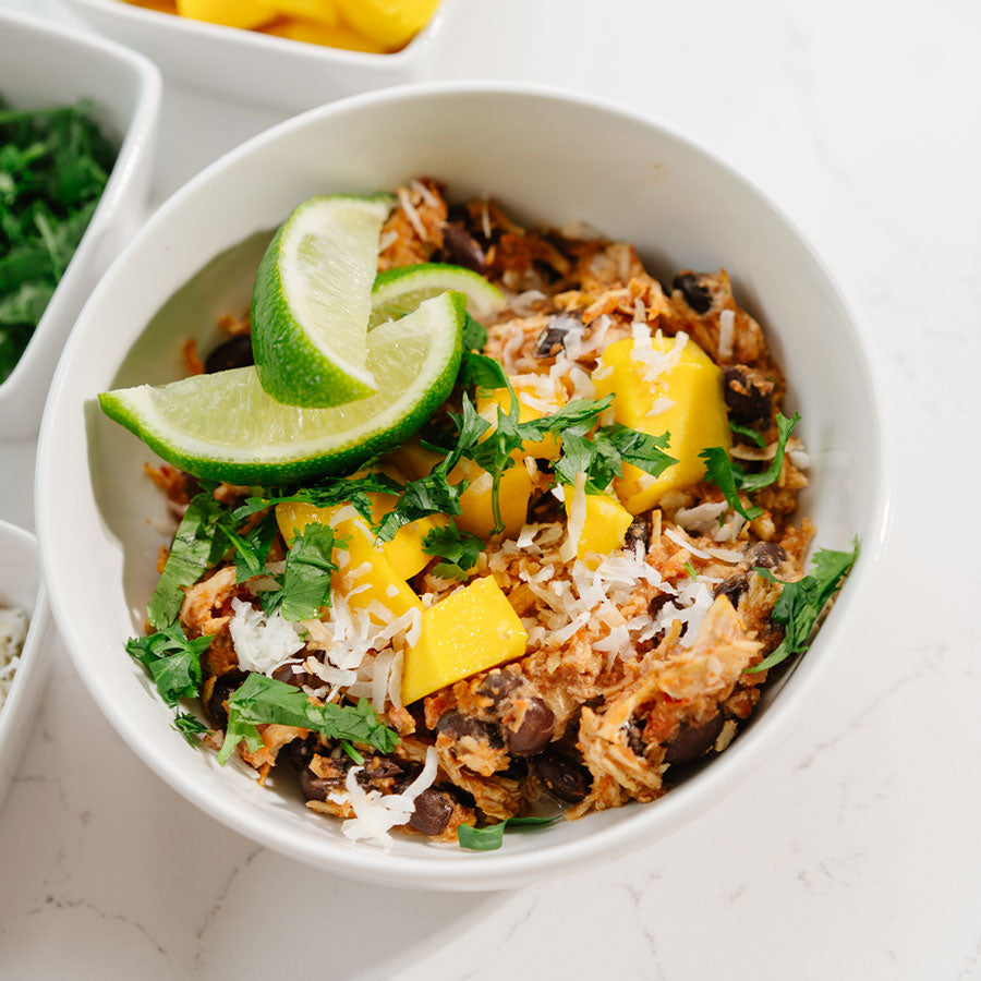 Bowl of Beehive Meals Chicken Burrito Bowls with lime wedges and mangoes on a white surface