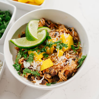 Bowl of Beehive Meals Chicken Burrito Bowls with lime wedges and mangoes on a white surface