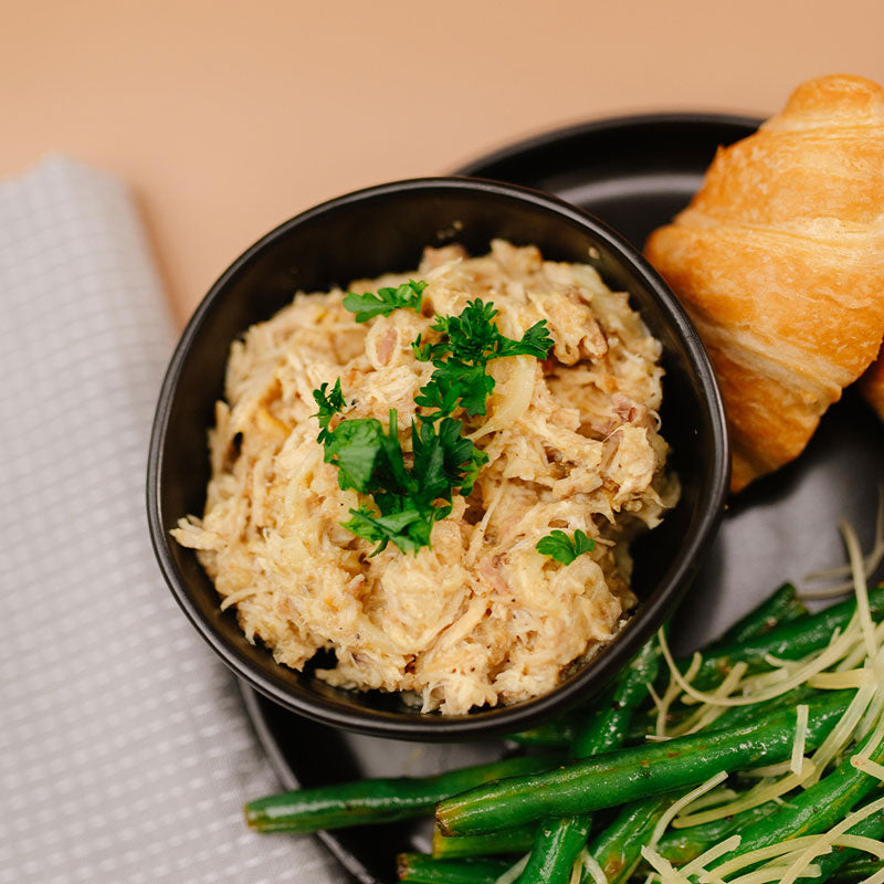 Bowl of chicken with croissant, and green beans on a plate.