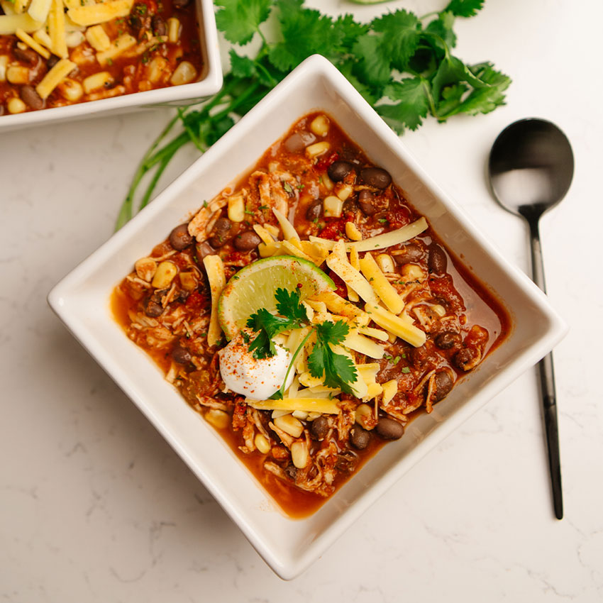  bowl of Beehive Meals Chicken Enchilada Soup with cheese, lime, and cilantro on a white surface