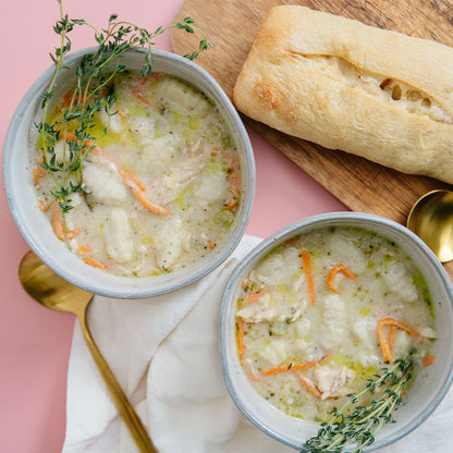 Two bowls of soup with a loaf of bread on a pink background