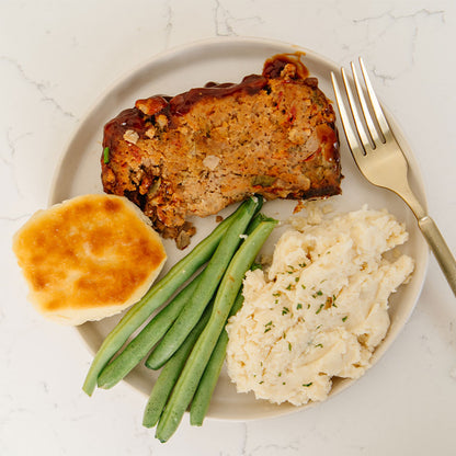 Plate of Beehive Meals Classic Meatloaf, green beans, mashed potatoes, and a biscuit on a white plate with a fork.