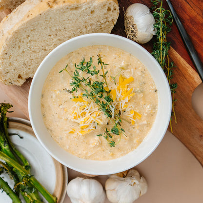 Bowl of soup with herbs and cheese on a wooden board with bread and vegetables.