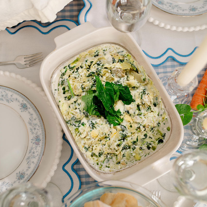 Spinach Artichoke dip on a table setting with plates and glasses.