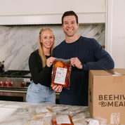 Two people holding a package of meat in a kitchen with a box labeled 'Beehive Meats' on a marble countertop.