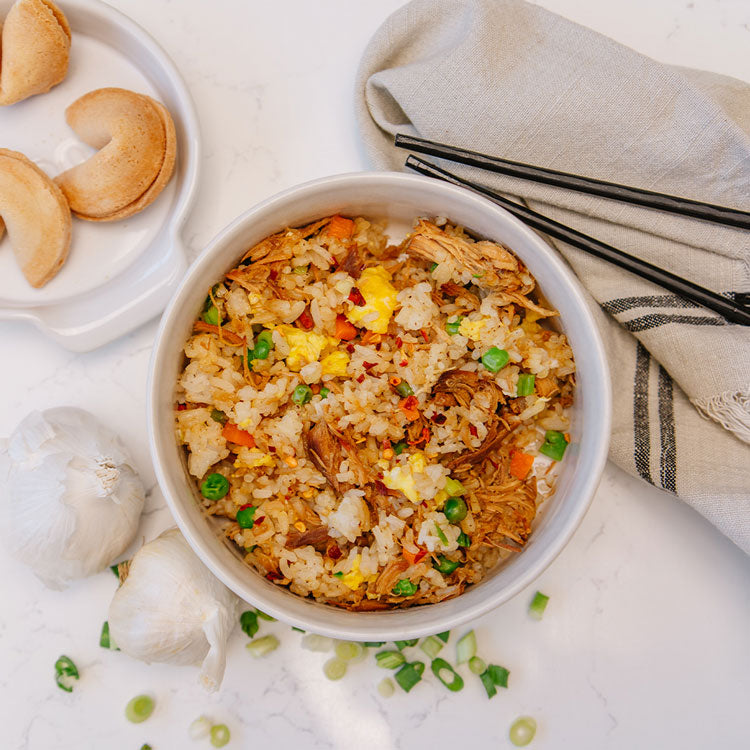 Fried rice dish in a white bowl with shredded chicken and fortune cookies on the side. 