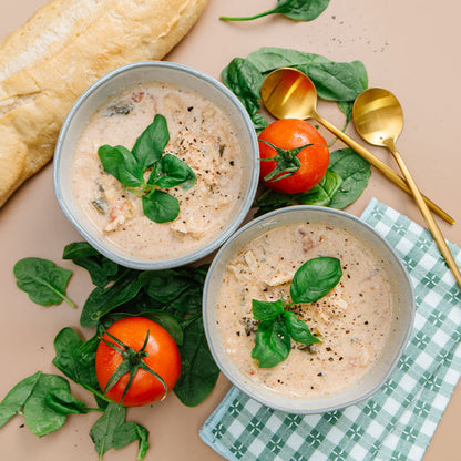 Two bowls of soup with bread, tomatoes, and spinach on a beige surface