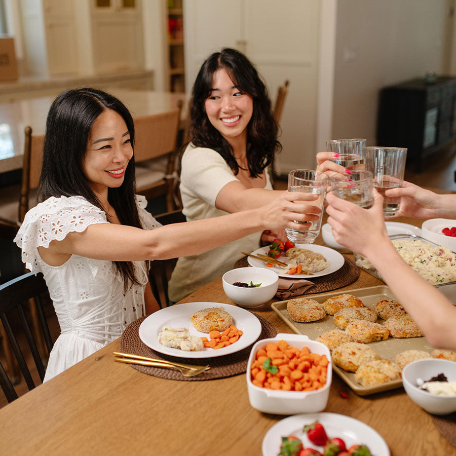 Two women toasting with glasses at a dinner table with food.