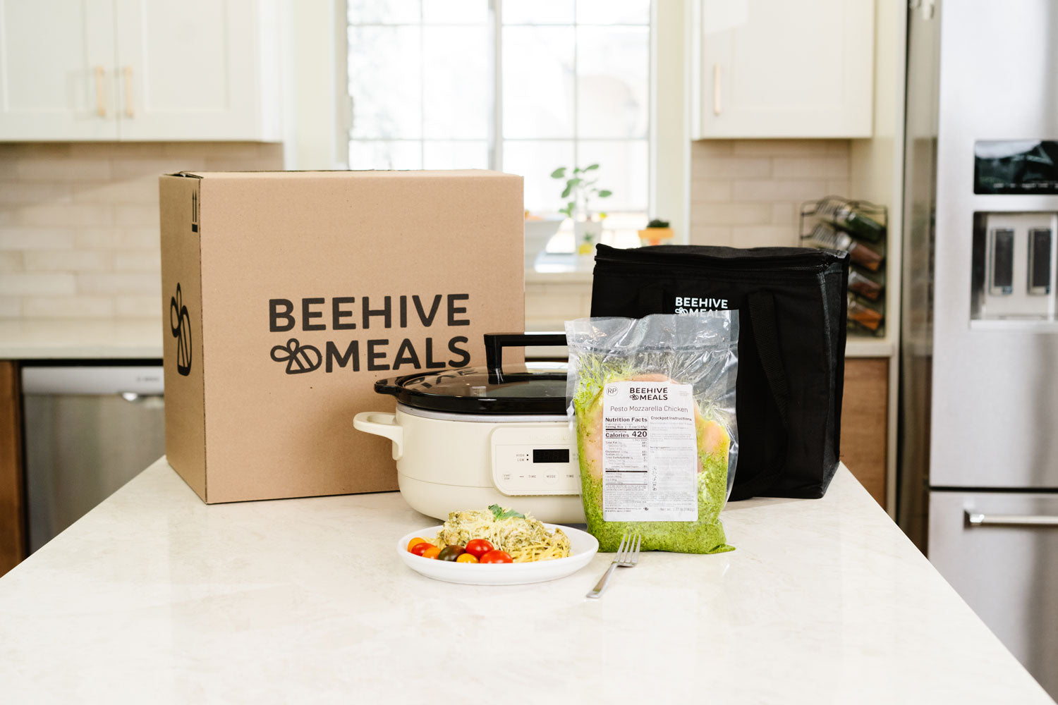 Beehive Meals packaging on a kitchen counter with a plated meal in front of a slow cooker.