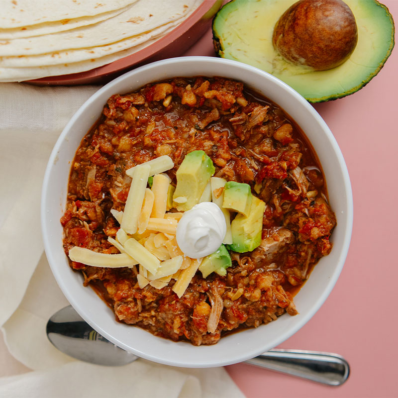 Bowl of chili with toppings on a pink background