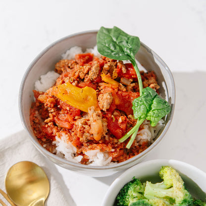 Bowl of food with ground sausage, vegetables, and rice on a white background