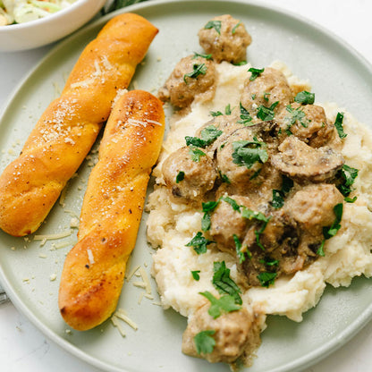 Plate of mashed potatoes with meatballs and bread sticks on a light background