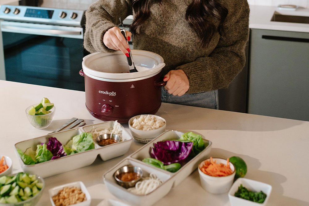 Person preparing a salad with a crock pot on a kitchen counter