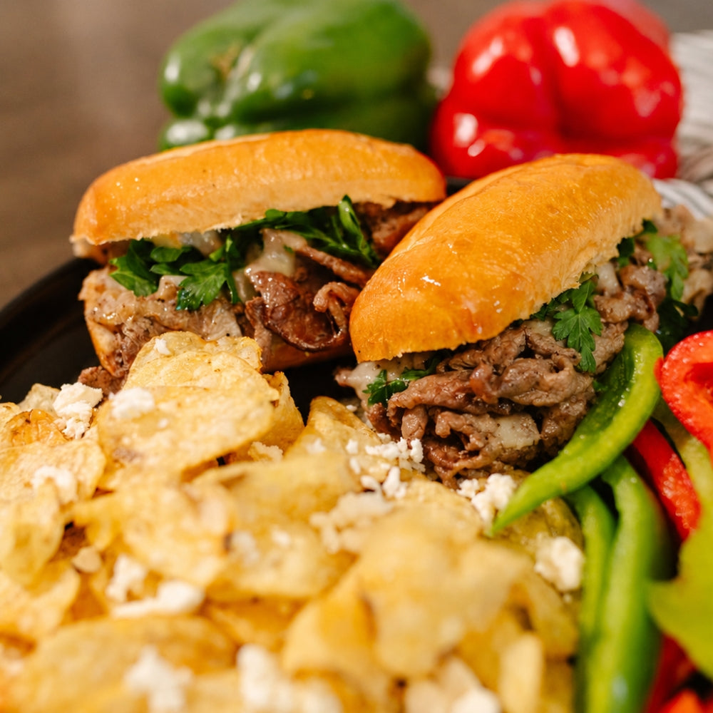 Close-up of a Philly Cheesesteak sandwich with meat and vegetables, accompanied by tortilla chips and bell peppers.