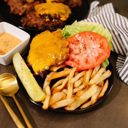 Beehive Meals BBQ Bacon Smash Burger with cheese, tomato, and pickle on a plate with fries and a side of sauce.