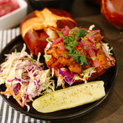 Plated BBQ Chicken Sandwich with pickled onions, cilantro, coleslaw, and a pickle on the side.