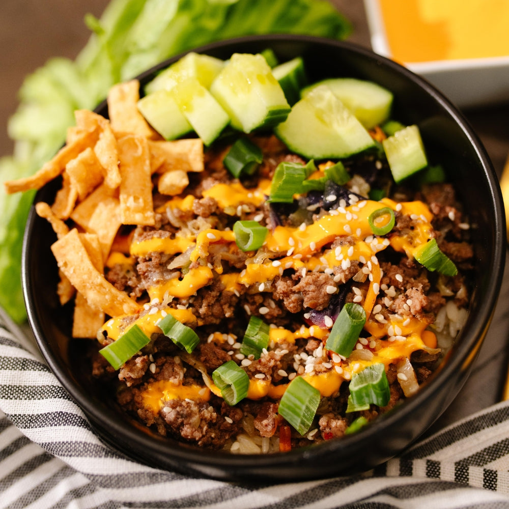 Black bowl filled with a Beehive Meals Egg Roll in a Bowl with wonton crisps, cucumber, and green onion. 