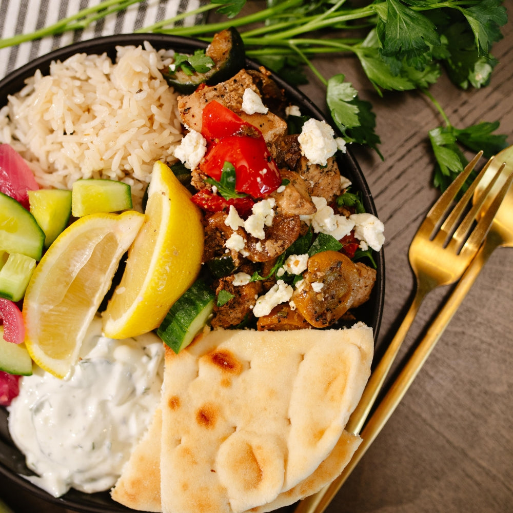 Plated dish with Beehive Meals Mediterranean Chicken, vegetables, lemon, rice, and naan bread on a wooden table.