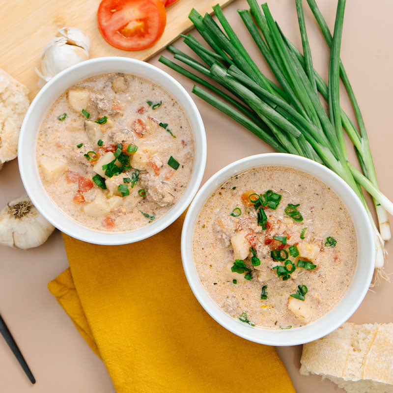 Two bowls of soup with garnishes on a table with vegetables and bread.