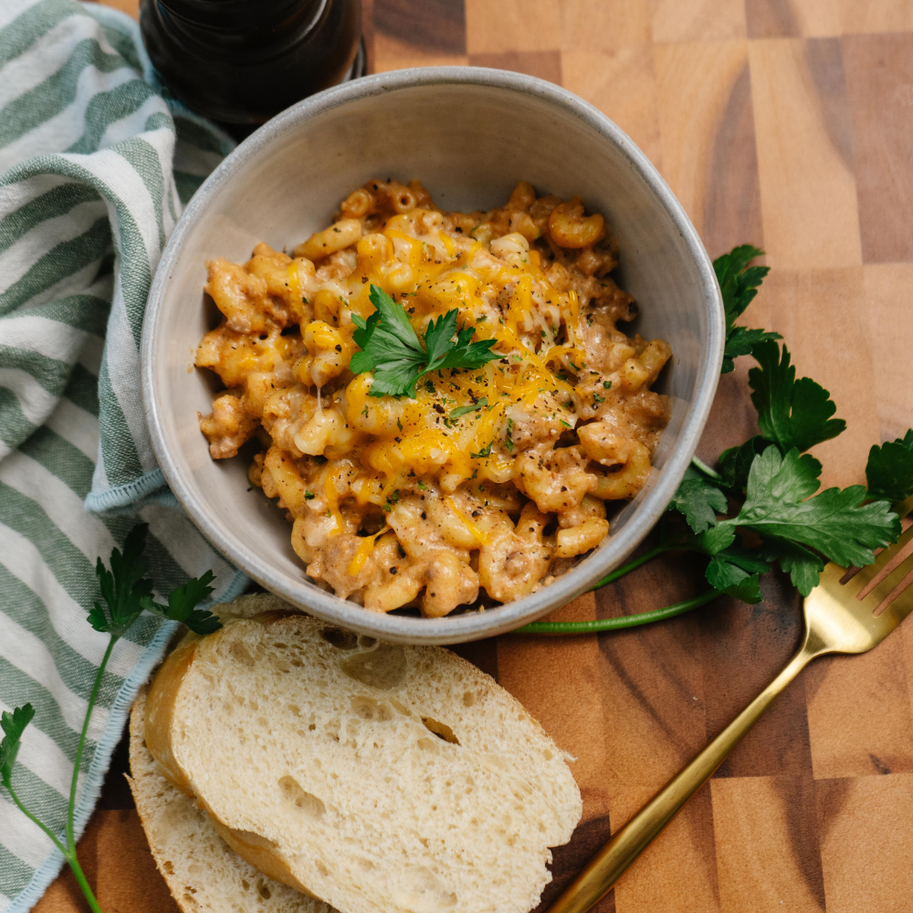 Bowl of macaroni and cheese with bread and a fork on a wooden surface