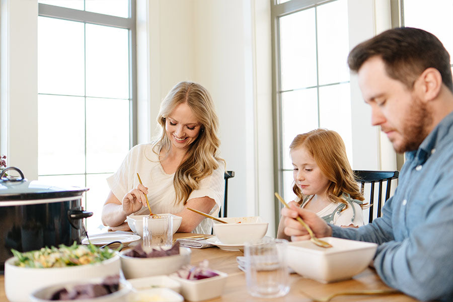 Family of three sitting at a dining table eating together.