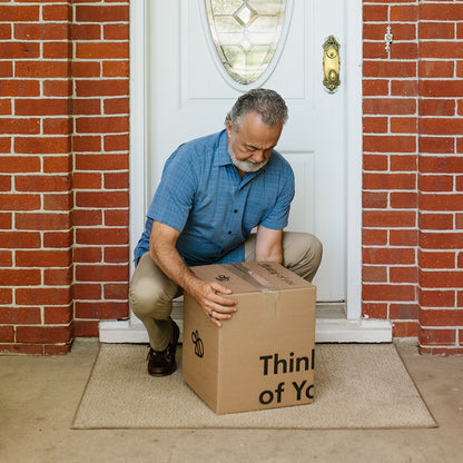 Man picking up a cardboard box in front of a door with a brick wall.