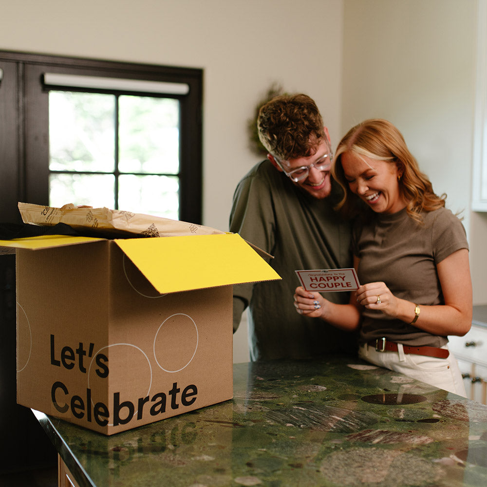 Two people in a kitchen with a 'Let's Celebrate' box and a 'Happy Couple' card.
