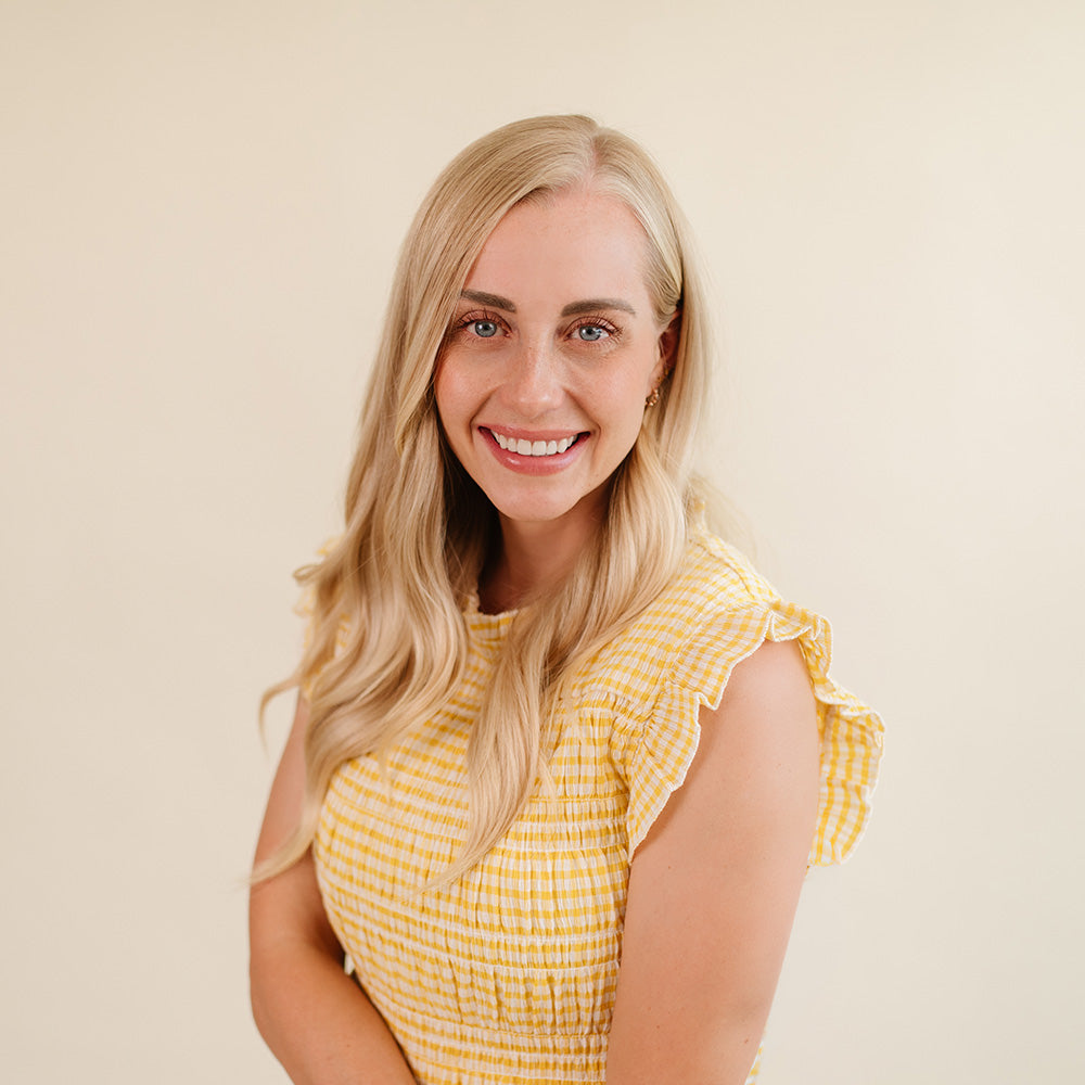 Beehive Meals Founder & CEO Allyse Jackson wearing a yellow and white gingham sleeveless top with ruffled shoulders, photographed against a plain warm beige background.